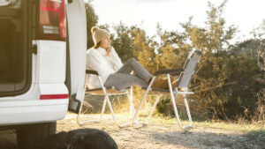 Femme assise au soleil en tenue d'hiver à côté d'un camping-car