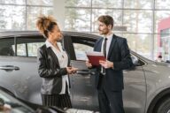 Cliente et vendeur automobile devant une voiture grise dans une concession