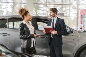 Cliente et vendeur automobile devant une voiture grise dans une concession