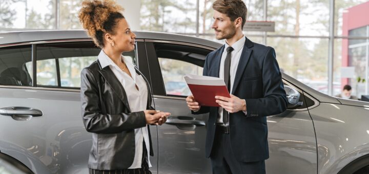 Cliente et vendeur automobile devant une voiture grise dans une concession